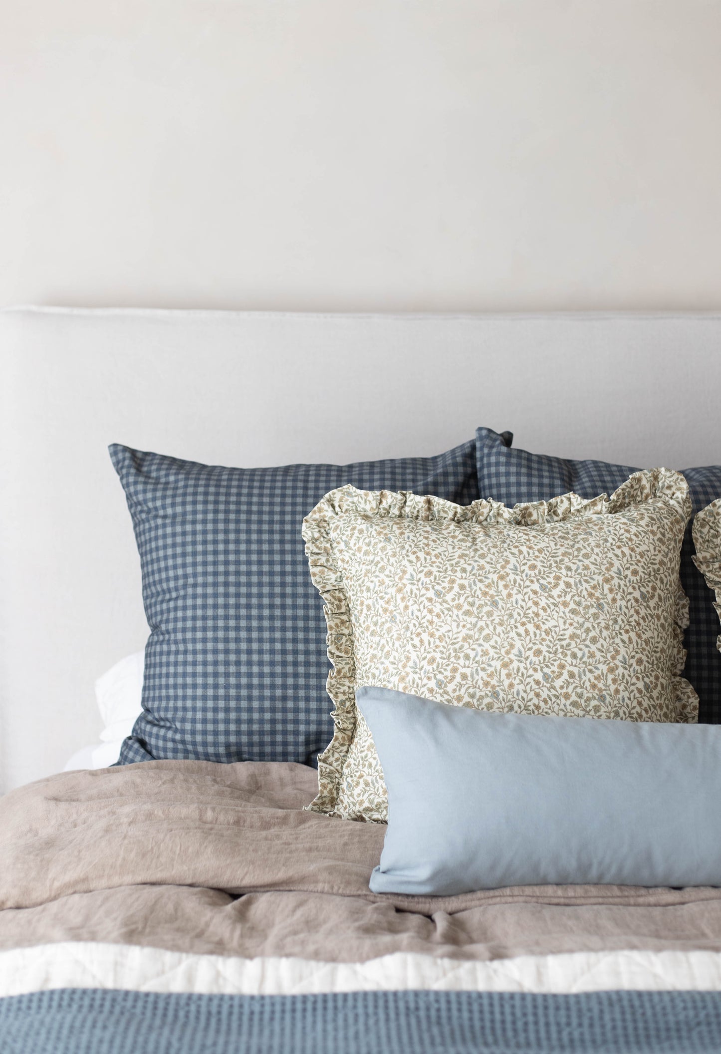 Navy and white gingham patterned pillow with button closure displayed on a bed.