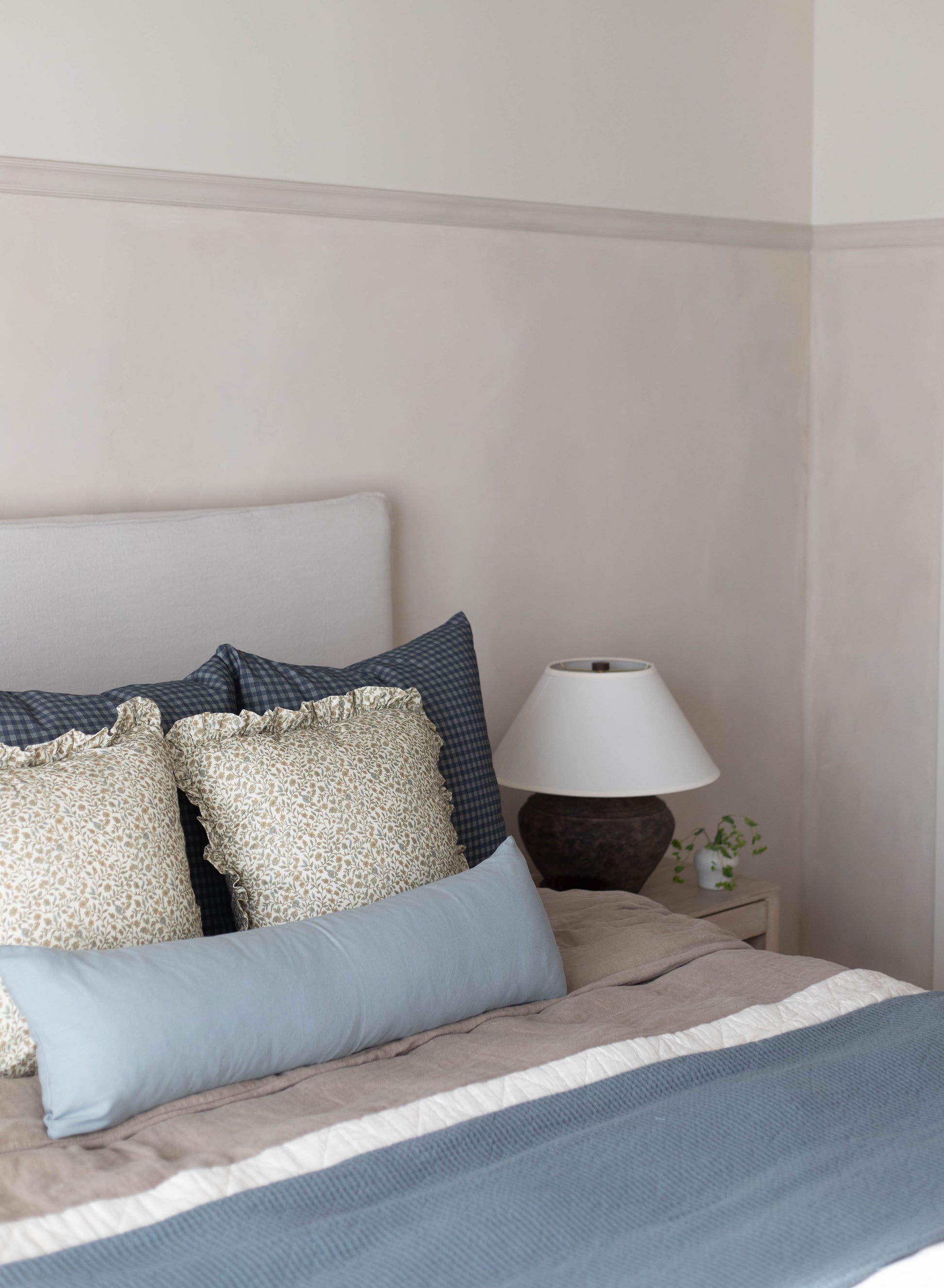 Navy gingham patterned pillow displayed on a bed with cream and blue bedding.