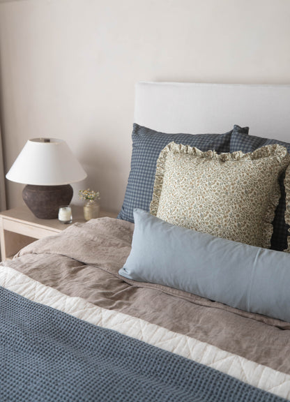 Navy and white gingham patterned pillow displayed on a bed with matching bedding and decorative pillows.