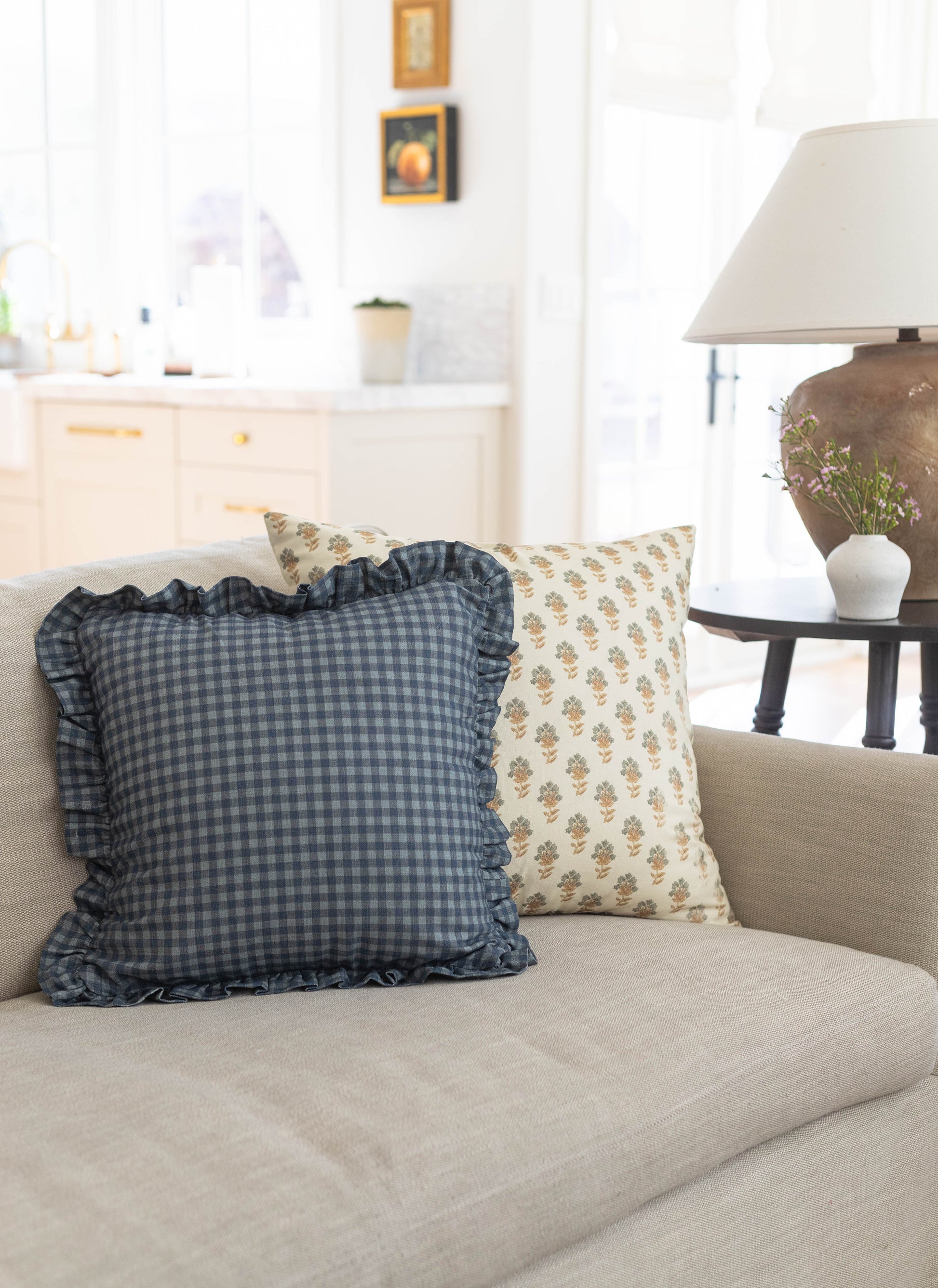 Navy gingham pillow with ruffled edges on beige sofa.