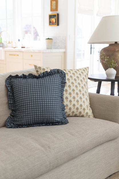 Navy gingham pillow with ruffle trim and cream floral pillow on beige sofa in bright living room.
