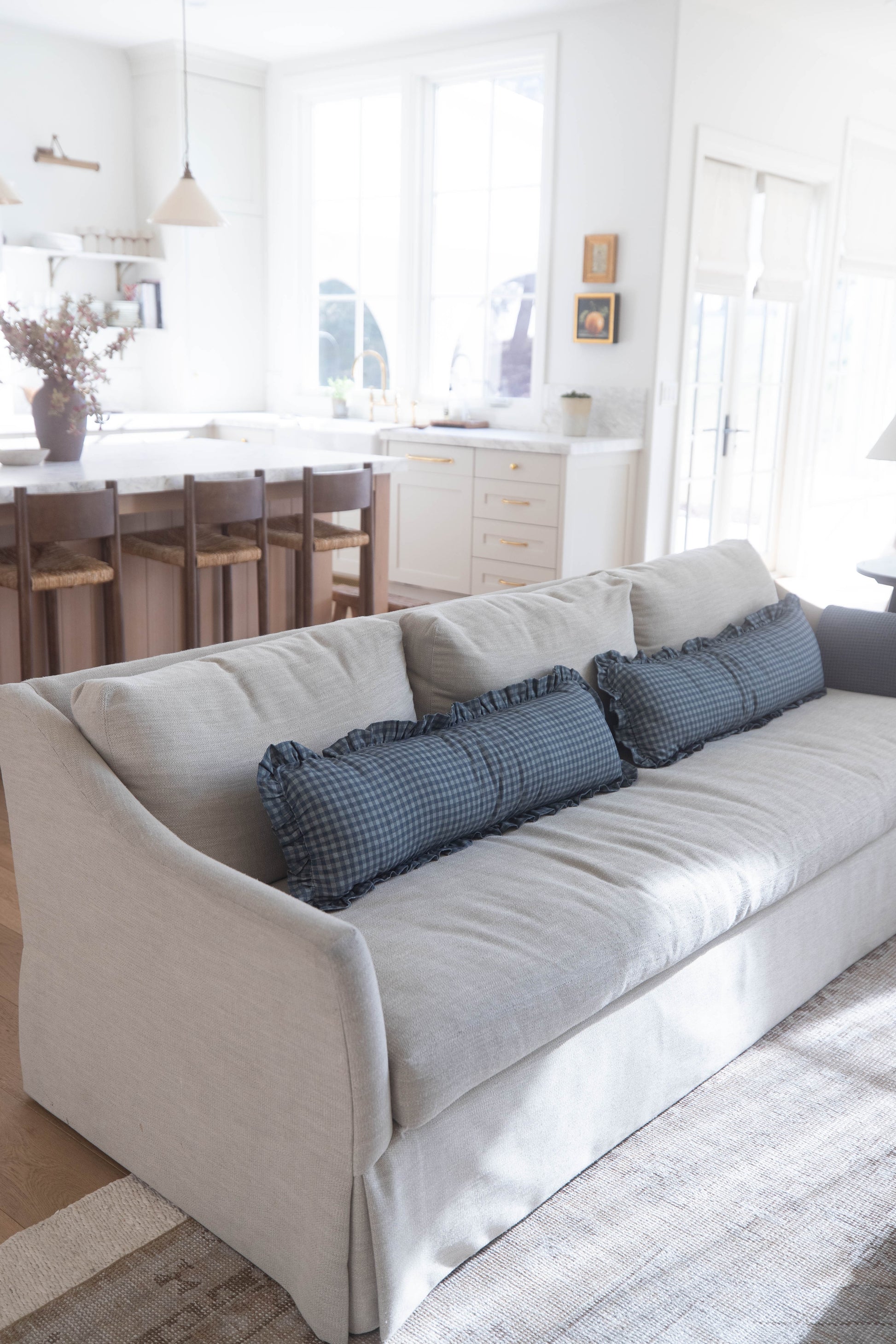 Navy gingham cylindrical pillows with ruffled edges arranged on a cream sofa.