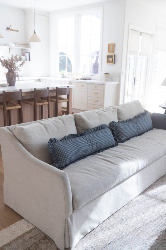 Navy gingham cylindrical pillows with ruffled edges arranged on a cream sofa.