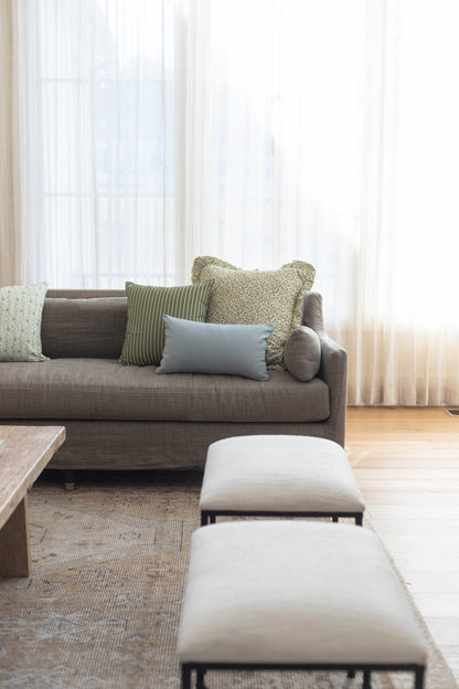 Gray upholstered sofa with decorative pillows in various patterns and textures arranged in a bright living room.