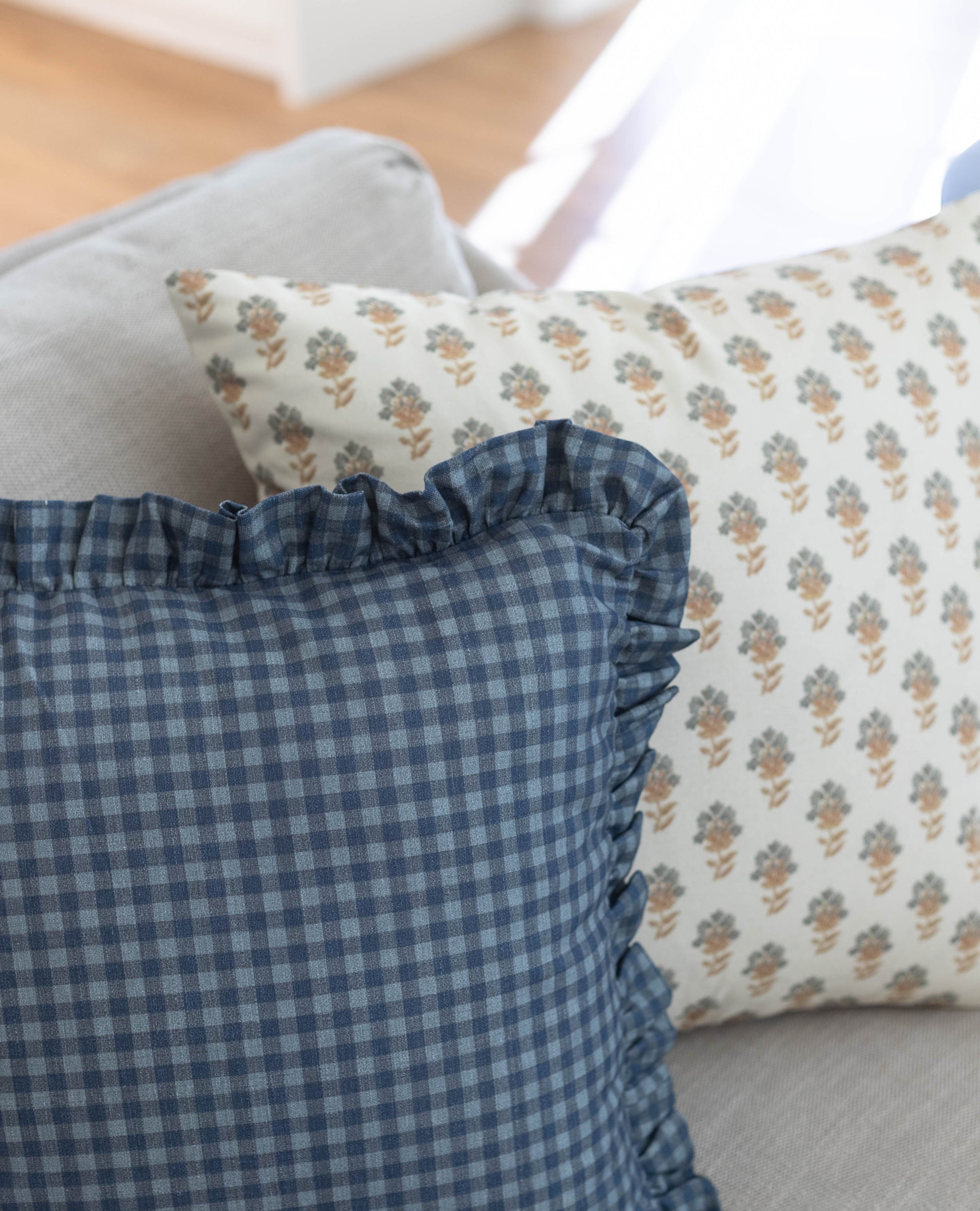 Navy gingham check pillow with ruffled edge displayed with a floral patterned pillow.
