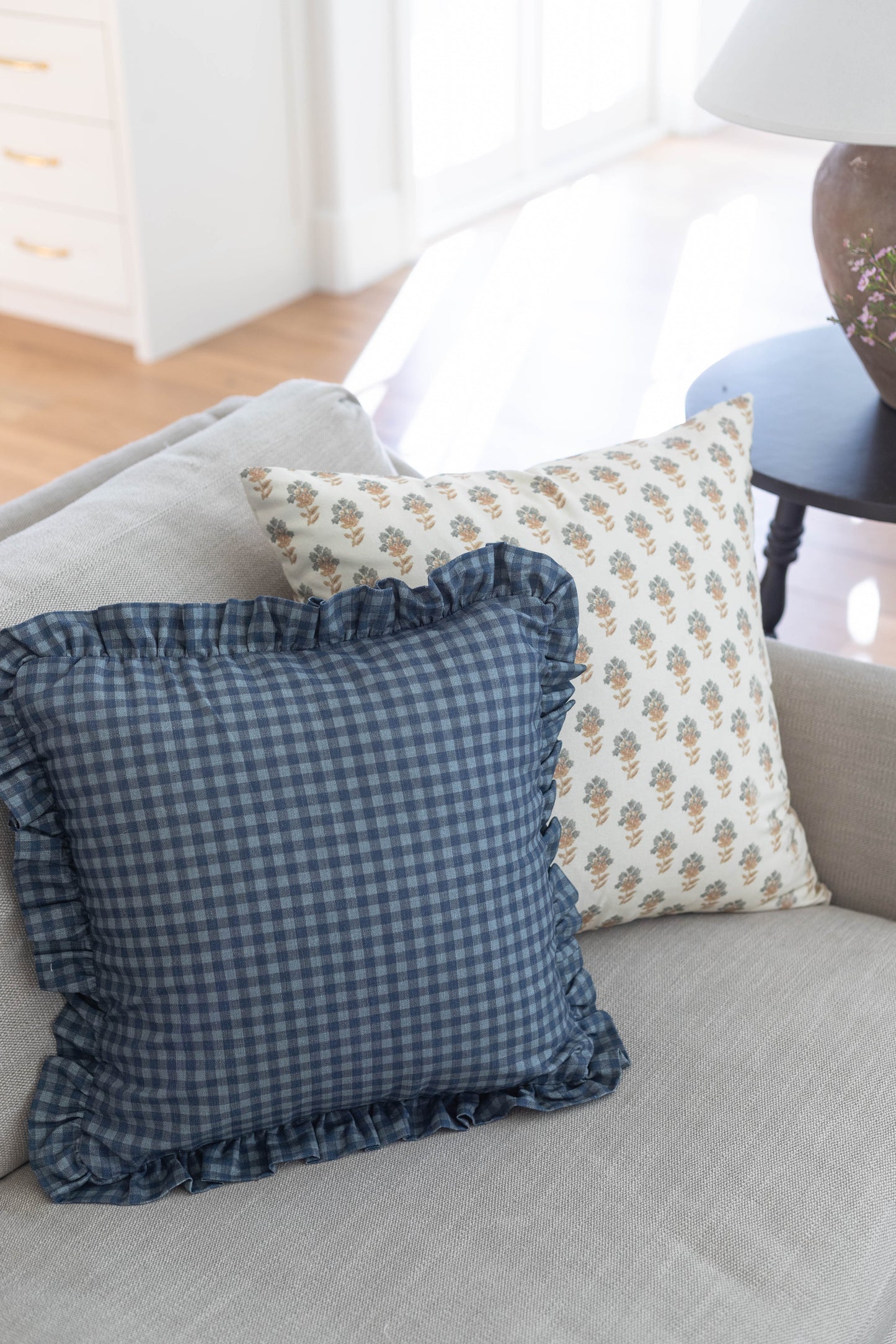 Navy gingham pillow with ruffled edges displayed on a gray sofa.