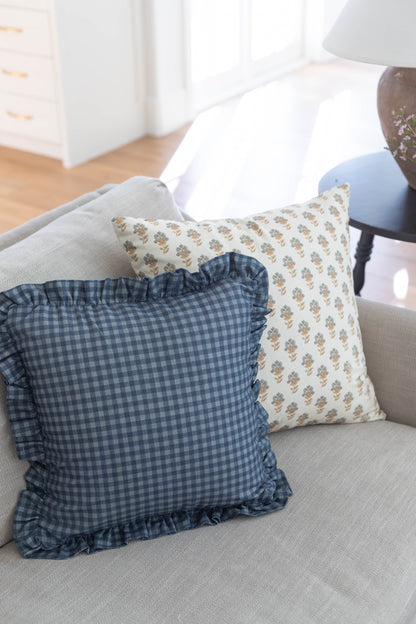 Navy gingham pillow with ruffled edges displayed on a gray sofa.