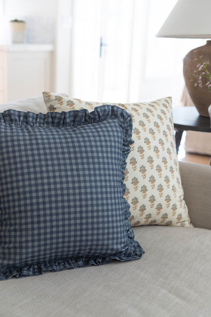 Navy gingham pillow with ruffled edges on beige sofa next to floral patterned pillow.