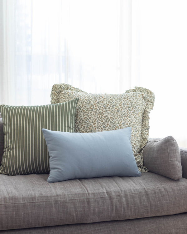 Blue rectangular lumbar pillow displayed on gray sofa with striped and patterned decorative pillows.
