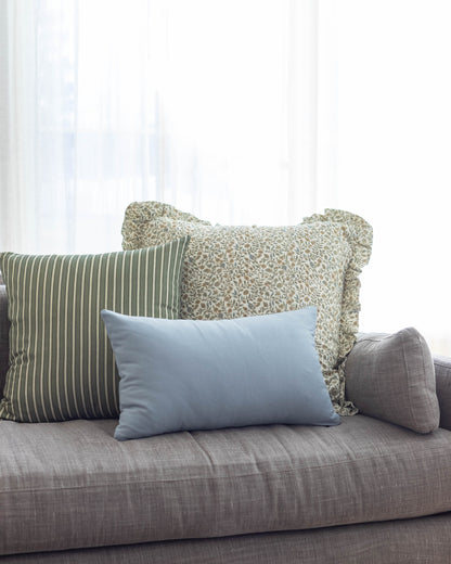 Meadow Ruffle pillow with ruffled edges in sage green floral pattern displayed on gray sofa with striped and solid blue pillo