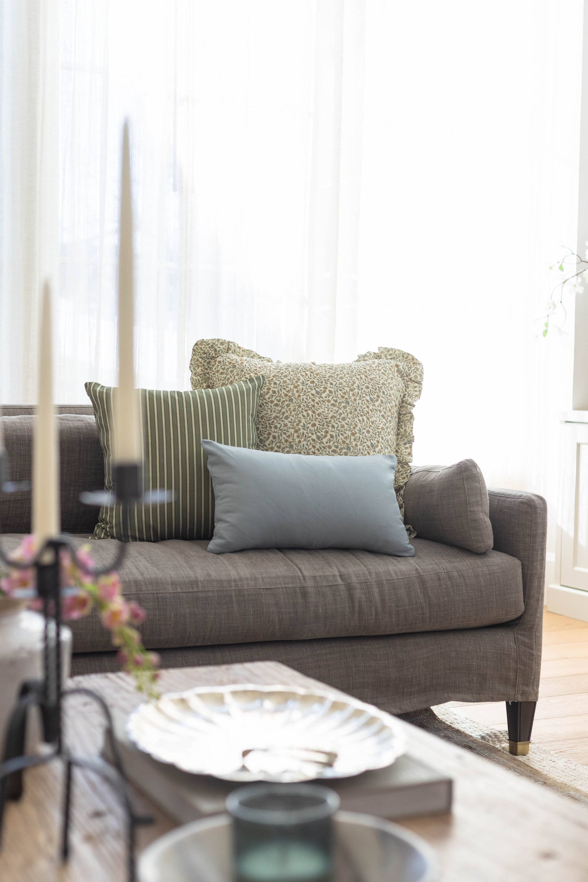 Gray linen pillow with ruffled edges displayed on a gray upholstered sofa with striped and textured accent pillows.