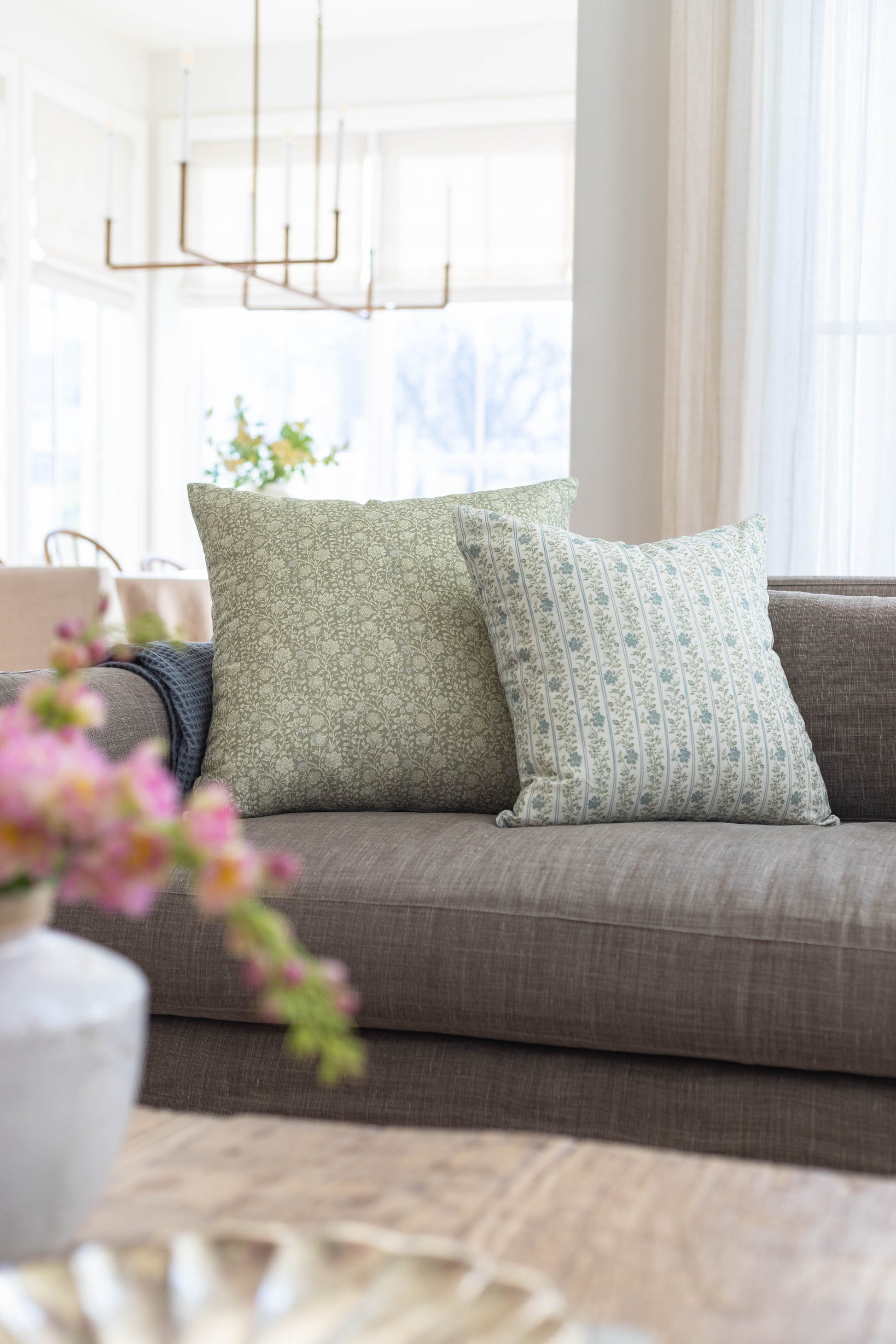 Two decorative pillows with green textured and patterned fabrics displayed on a gray upholstered sofa.