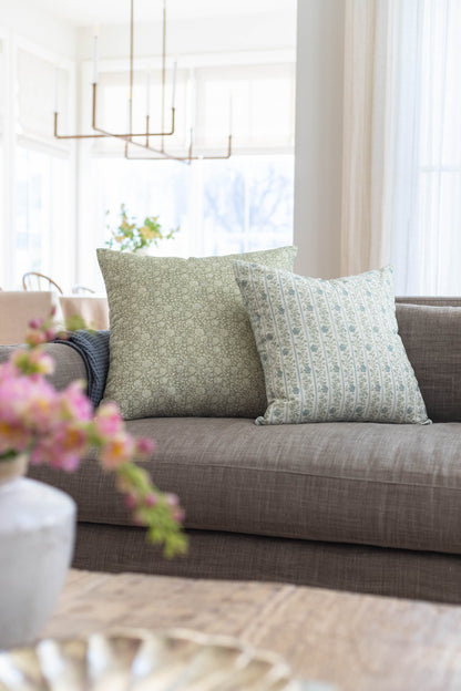 Two decorative pillows with green textured and patterned fabrics displayed on a gray upholstered sofa.