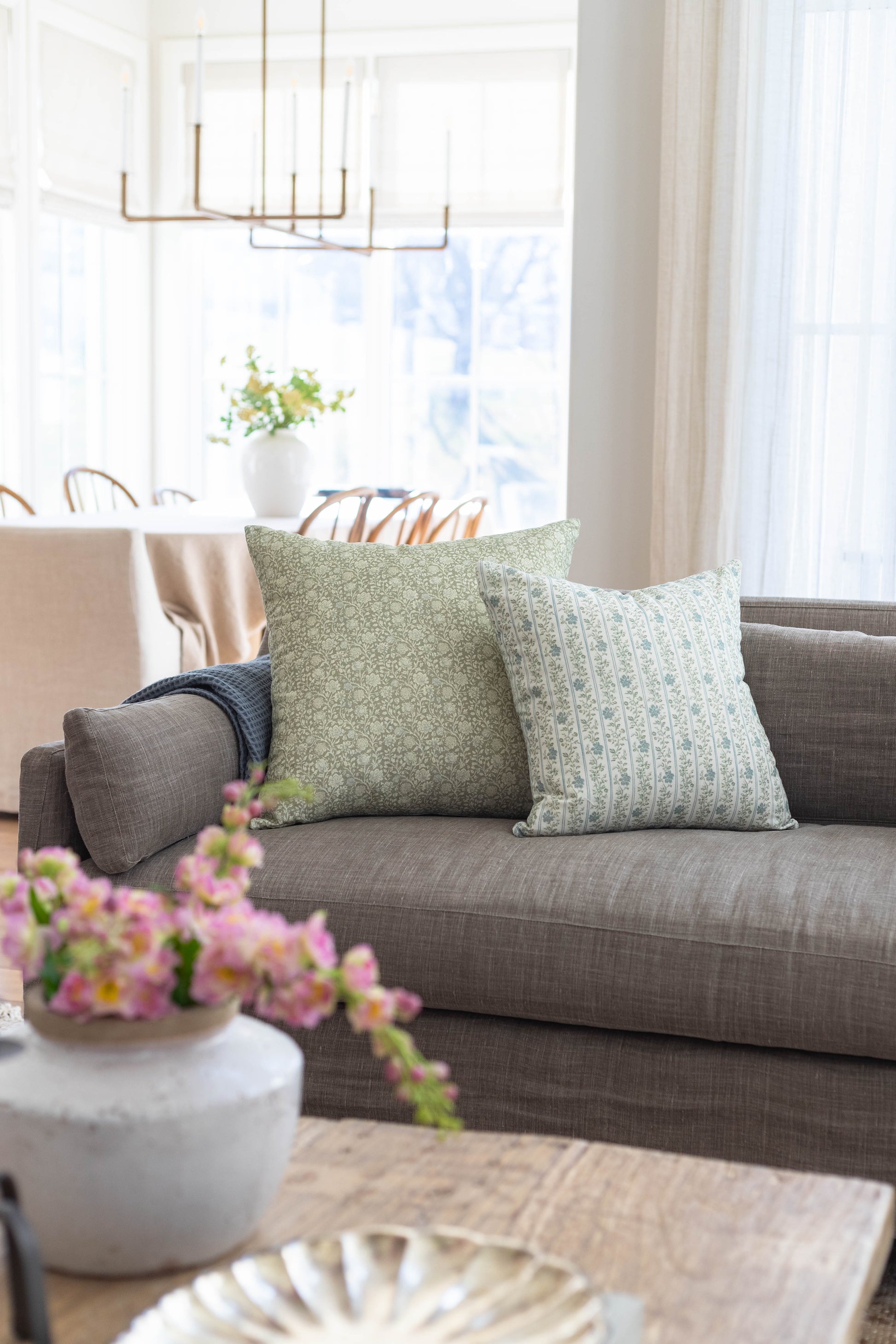 Two decorative pillows with green and blue patterns on gray upholstered sofa.