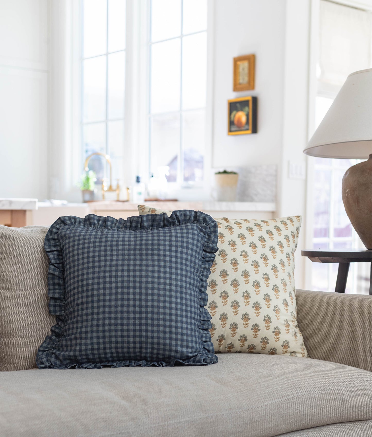 Navy blue gingham pillow with ruffled edges displayed on a cream-colored sofa.