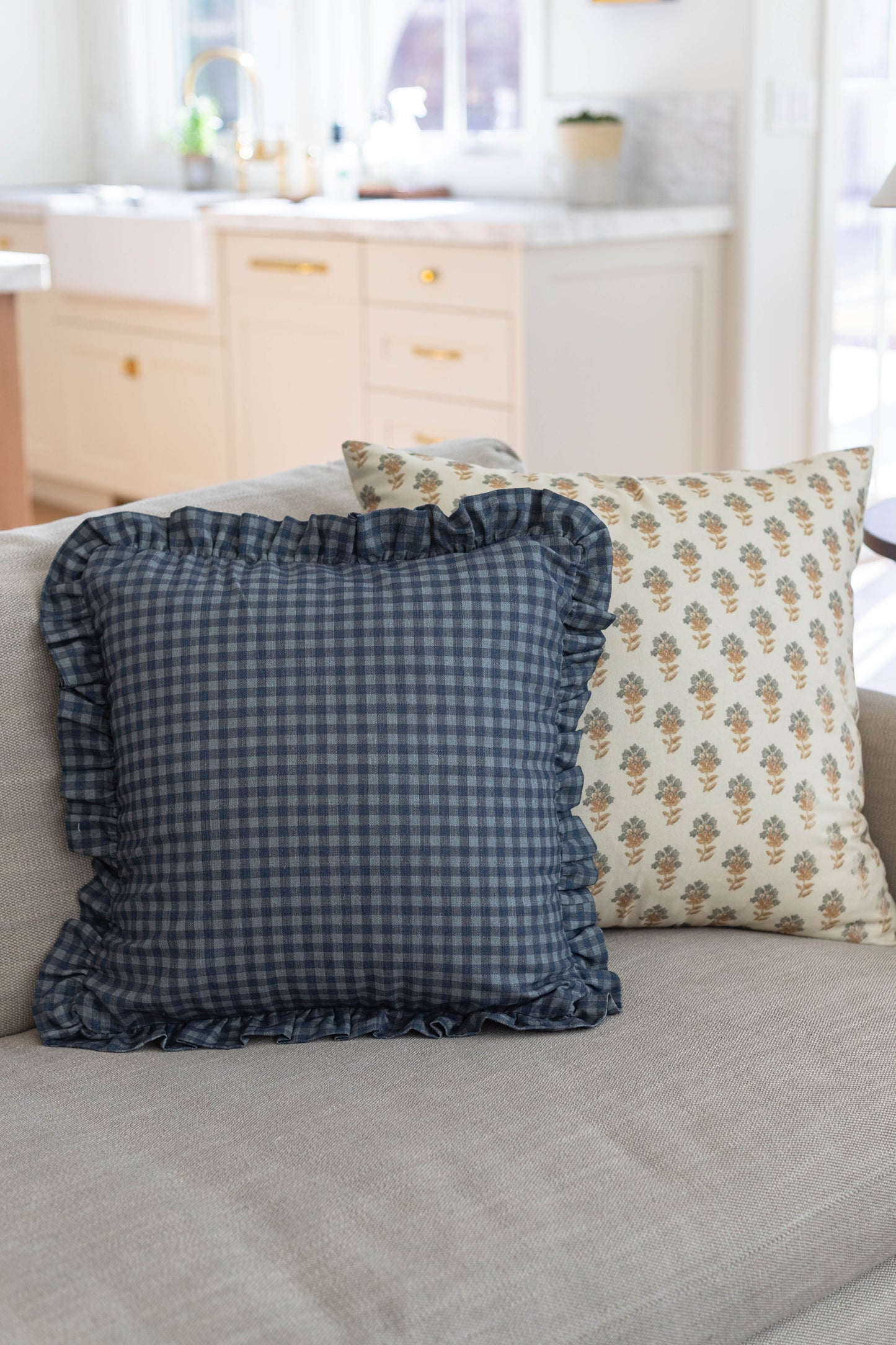 Navy gingham pillow with ruffled edges and floral patterned pillow on light gray sofa.