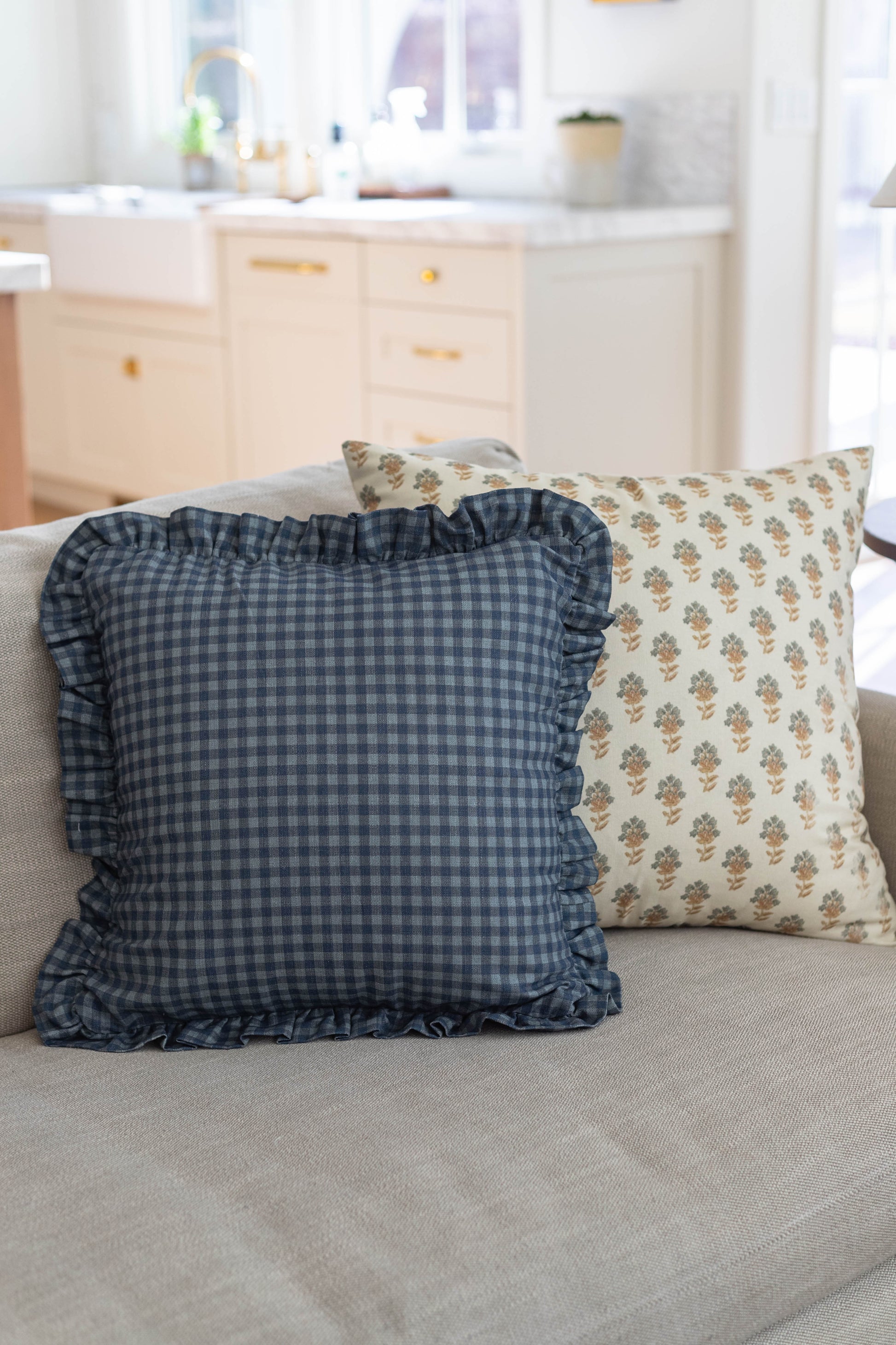 Navy gingham pillow with ruffled edges and floral patterned pillow on light gray sofa.