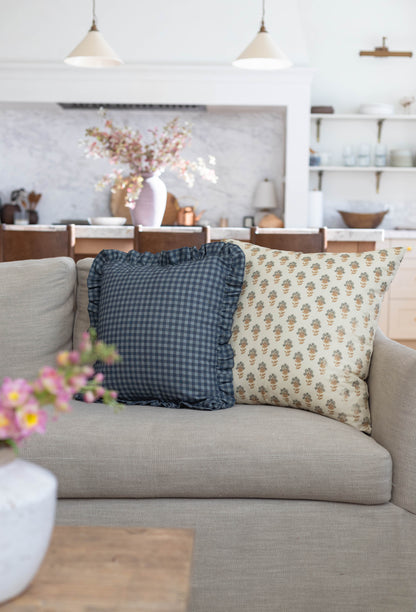 Two decorative pillows on a beige sofa: one navy gingham with ruffled edges, one cream with small floral print.