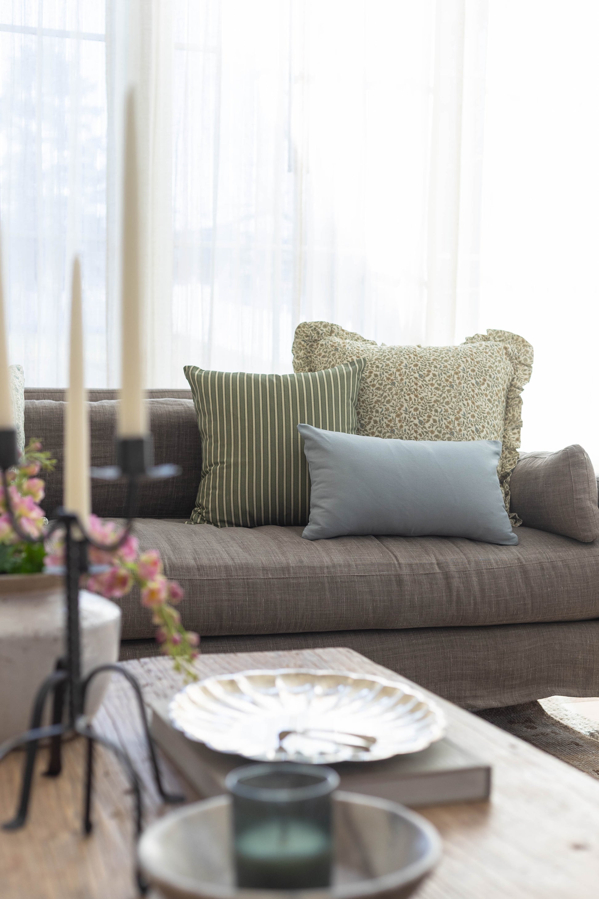 Gray sofa with green striped and patterned throw pillows and a light blue rectangular pillow in a bright living room.
