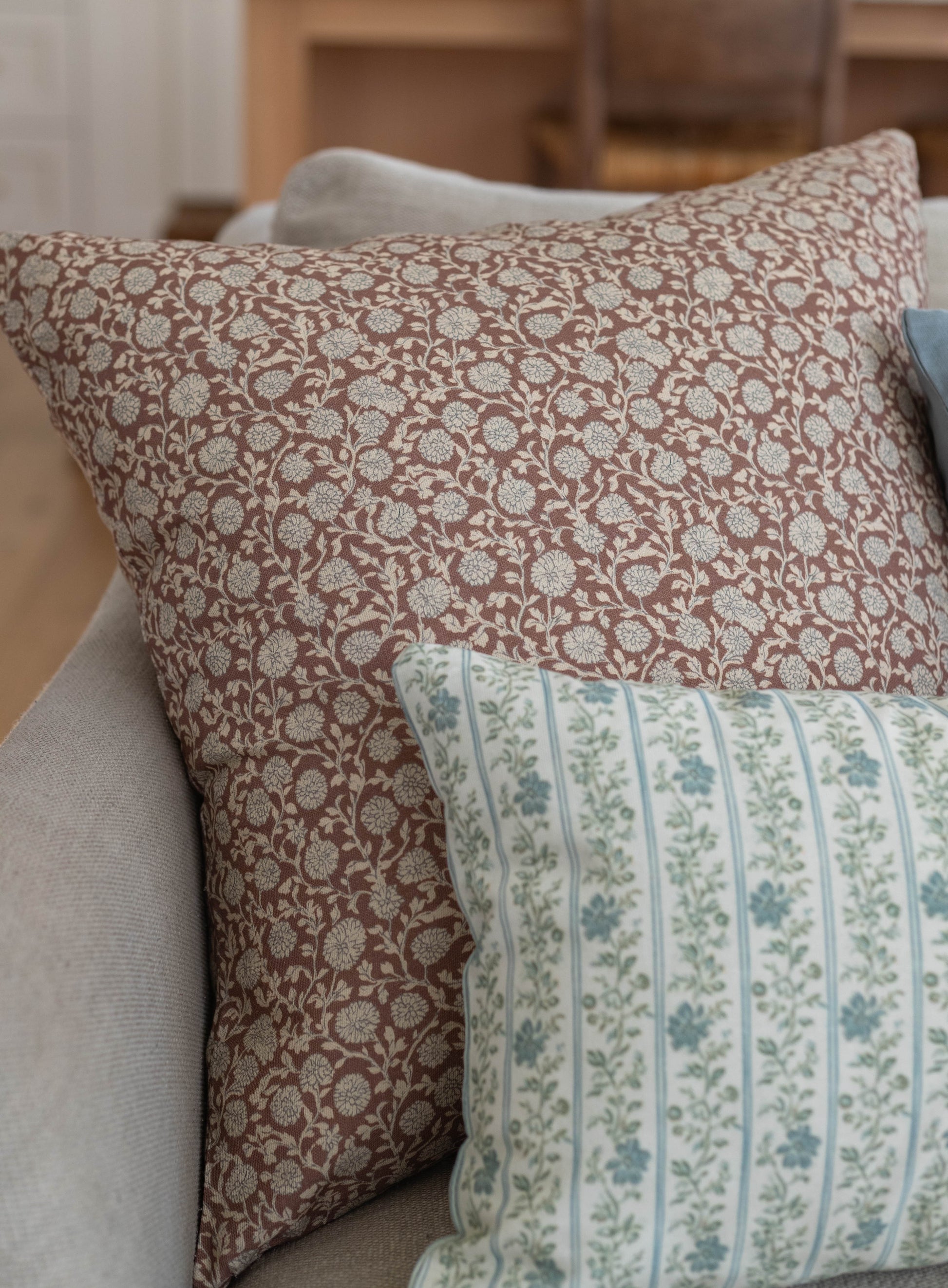 Throw pillow with tan background and cream floral damask pattern, displayed on upholstered furniture.