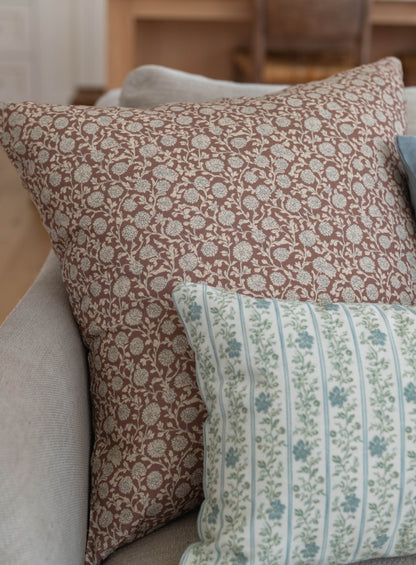 Throw pillow with tan background and cream floral damask pattern, displayed on upholstered furniture.