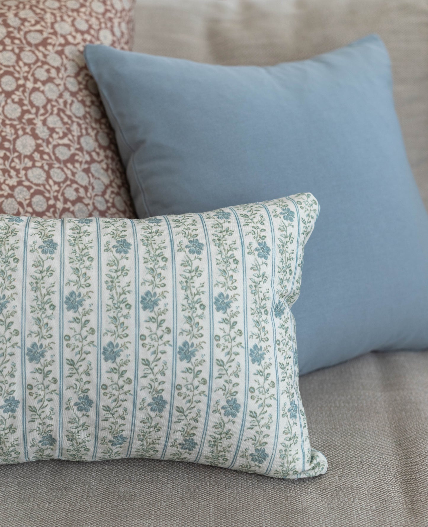 Rectangular lumbar pillow with cream background and blue-green floral striped pattern, displayed with solid blue and patterne