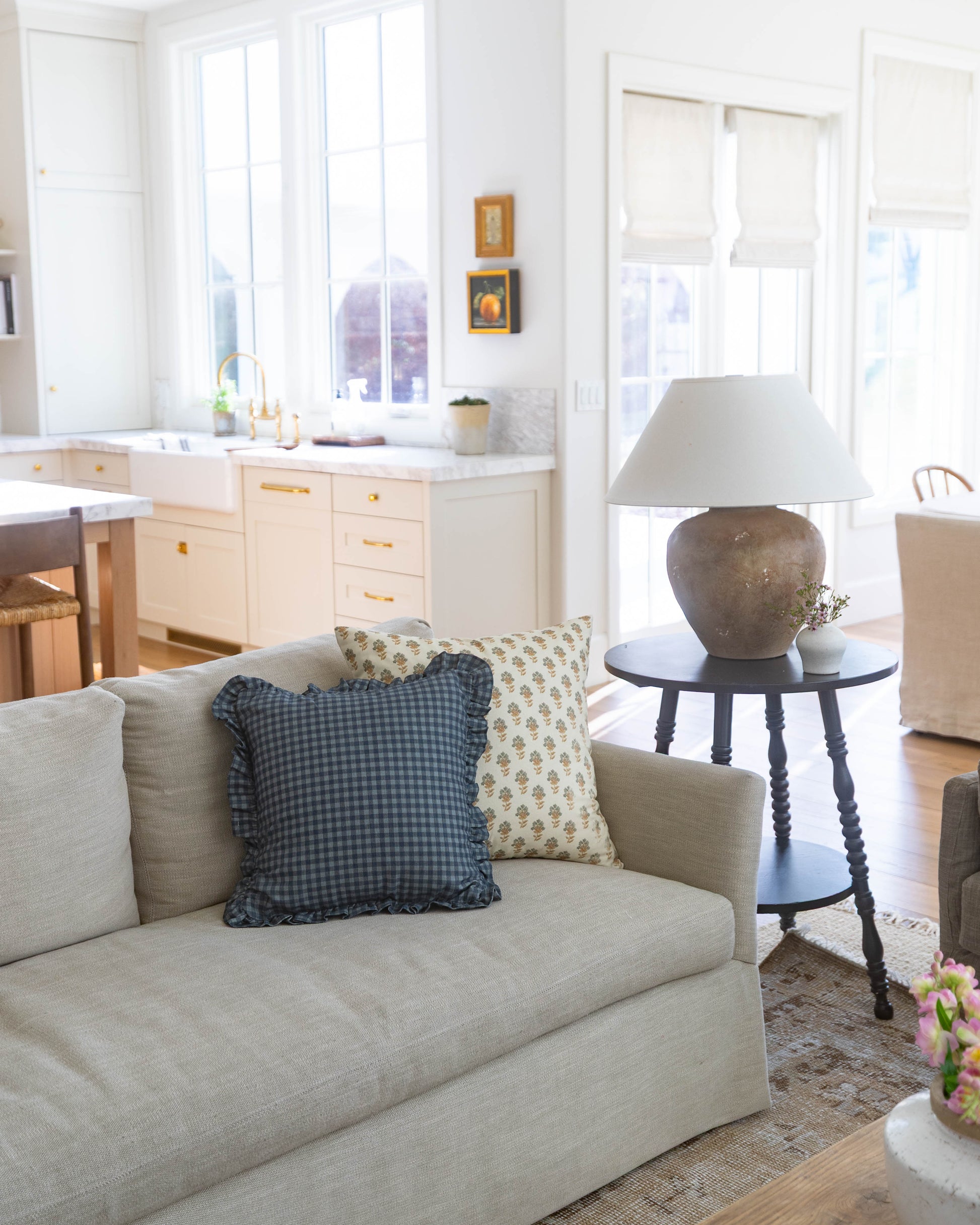Navy gingham pillow with ruffled edges displayed on a cream upholstered sofa.