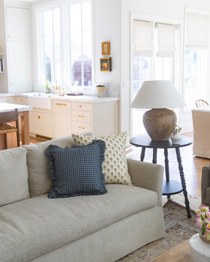 Navy gingham pillow with ruffled edges displayed on a cream upholstered sofa.