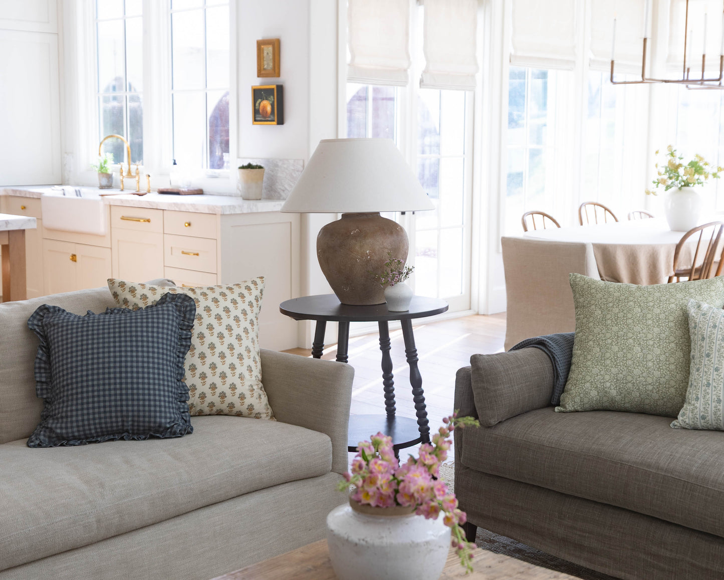 Two neutral-toned sofas with patterned and solid pillows face each other across a black side table holding a ceramic lamp.