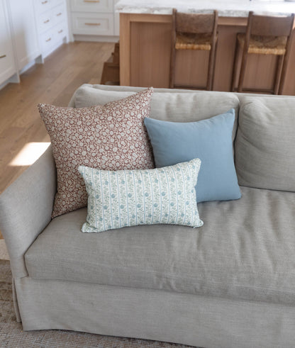 Three decorative pillows arranged on a beige upholstered sofa: brown floral, blue solid, and cream striped patterns.