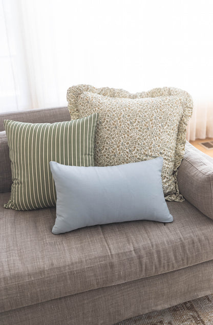 Three decorative pillows on a gray sofa: green striped, beige textured with ruffle trim, and light blue solid.