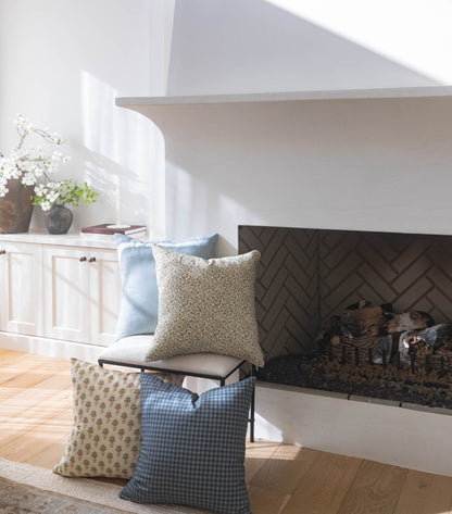 Navy gingham patterned pillow displayed with coordinating pillows in a bright living room setting near a fireplace.
