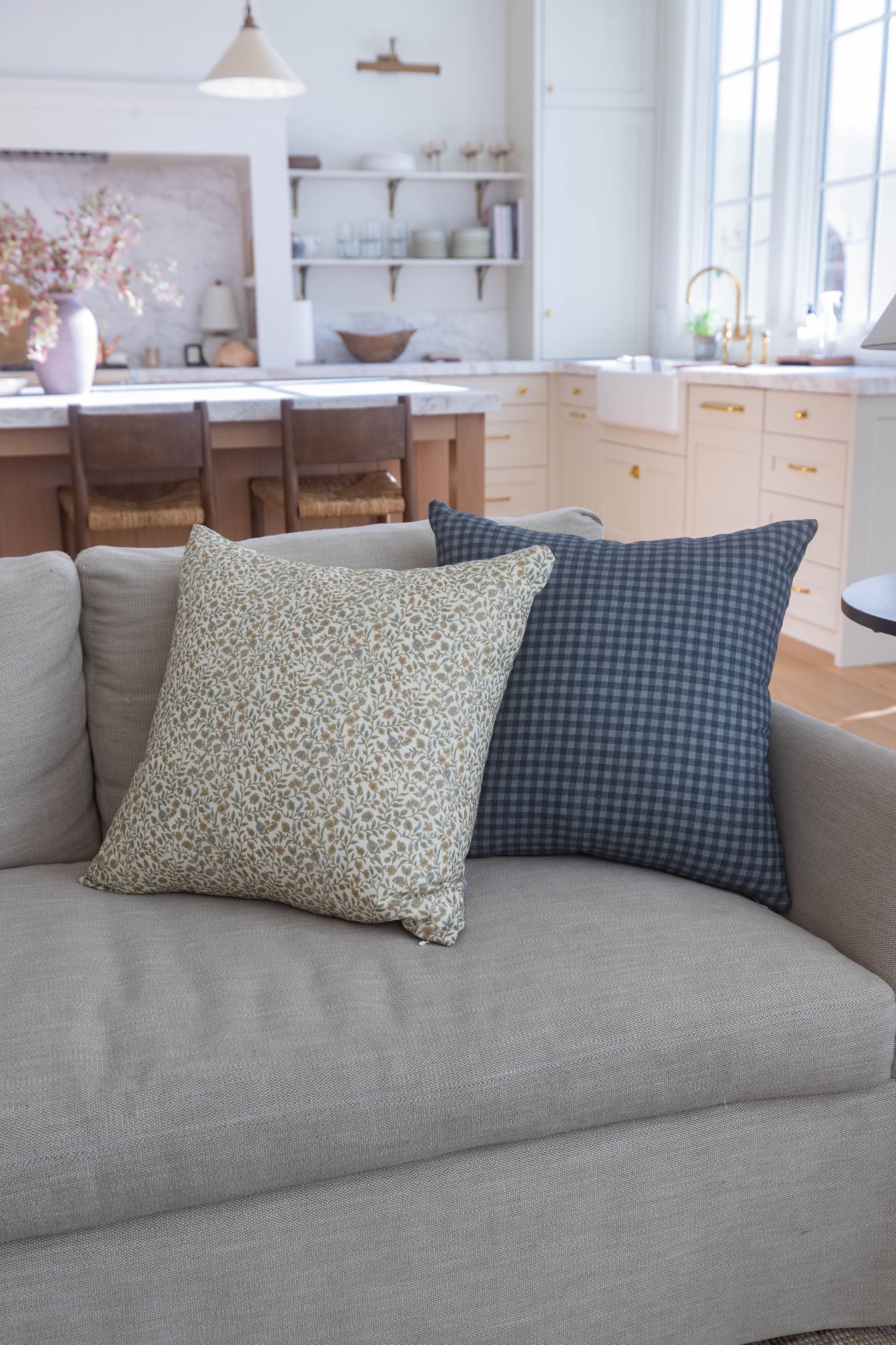 Two decorative pillows on a gray sofa: one with beige leaf pattern, one with dark blue gingham check.