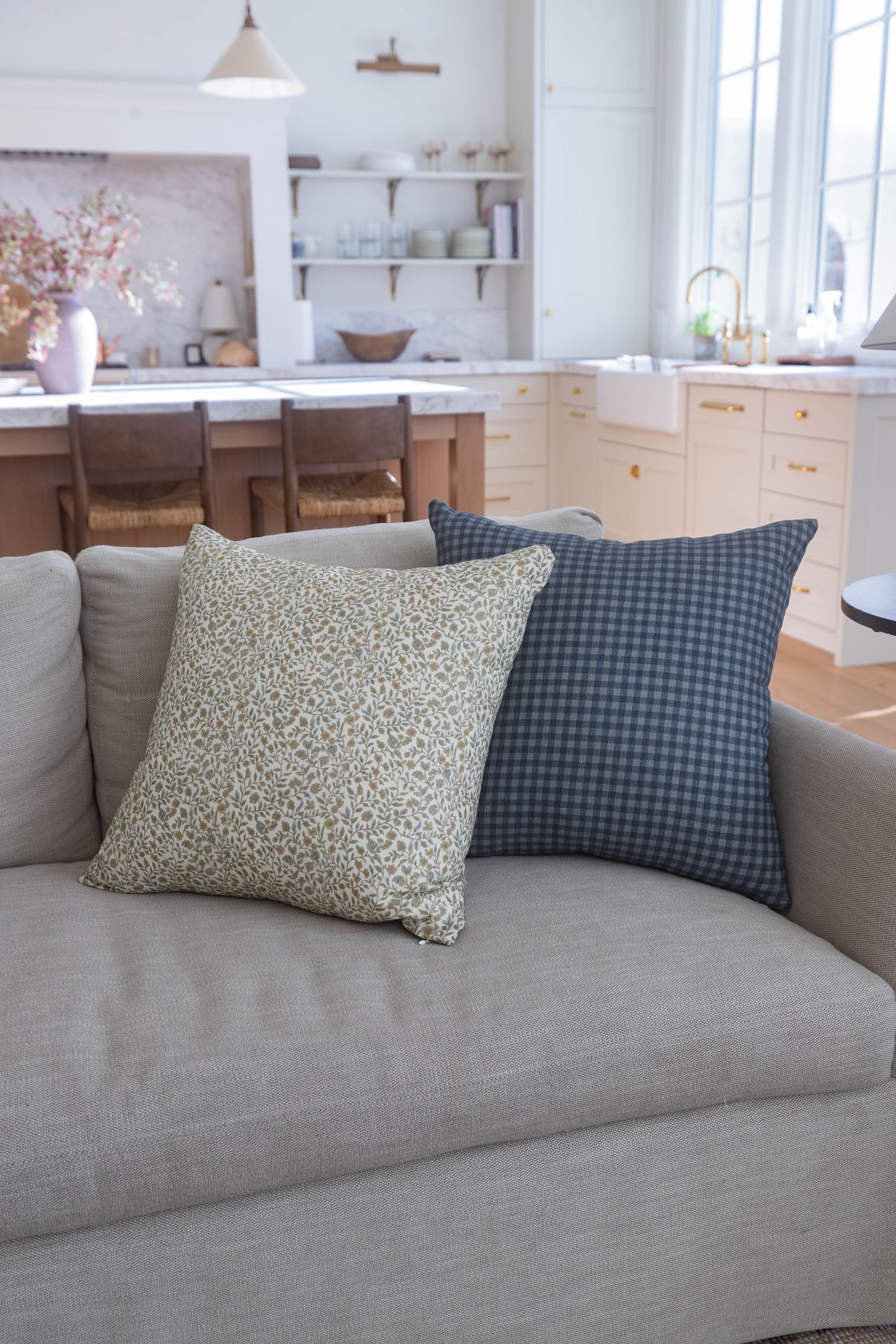 Navy gingham patterned square pillow on gray upholstered sofa in kitchen setting.