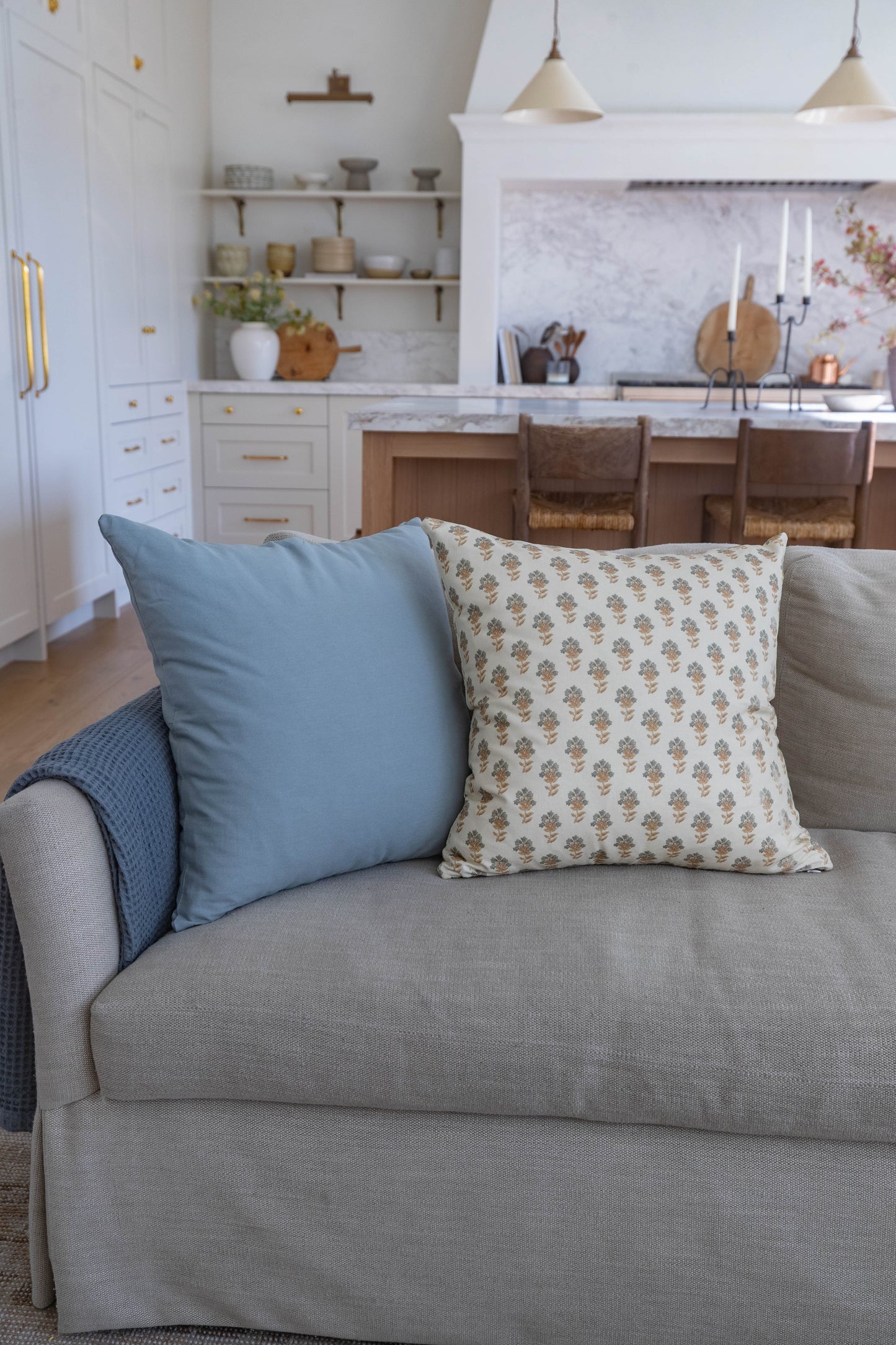 Blue and patterned throw pillows arranged on a gray upholstered sofa in a kitchen setting.