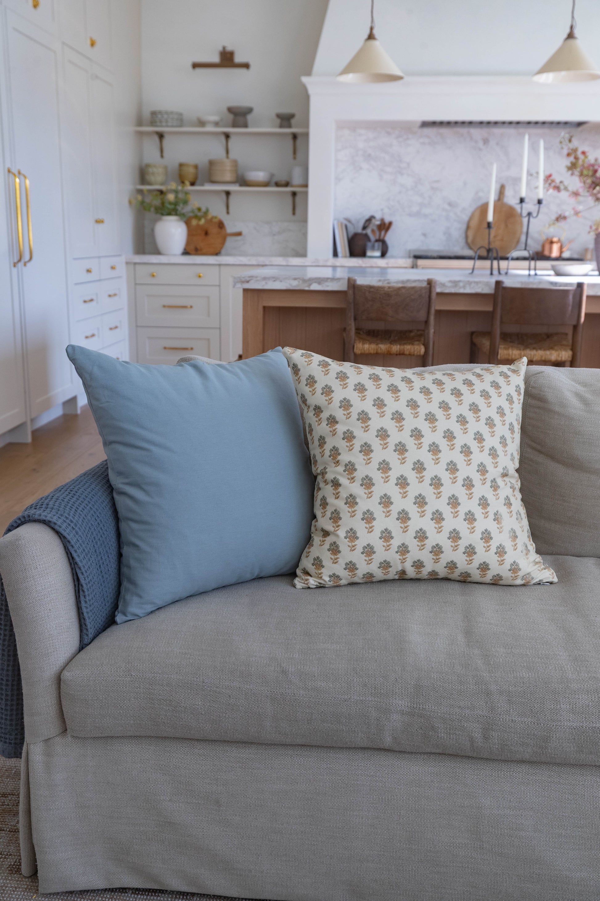 Blue and patterned throw pillows arranged on a gray upholstered sofa in a kitchen setting.