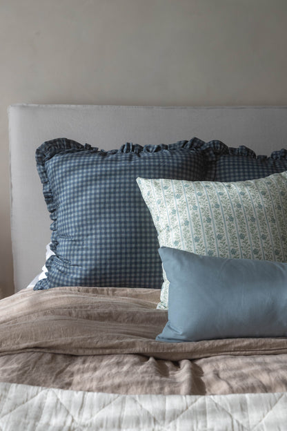 Navy gingham pillow with ruffled edges displayed on a bed with other decorative pillows.