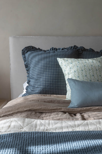 Navy gingham pillow with ruffled edges arranged on a bed with other decorative pillows and bedding.