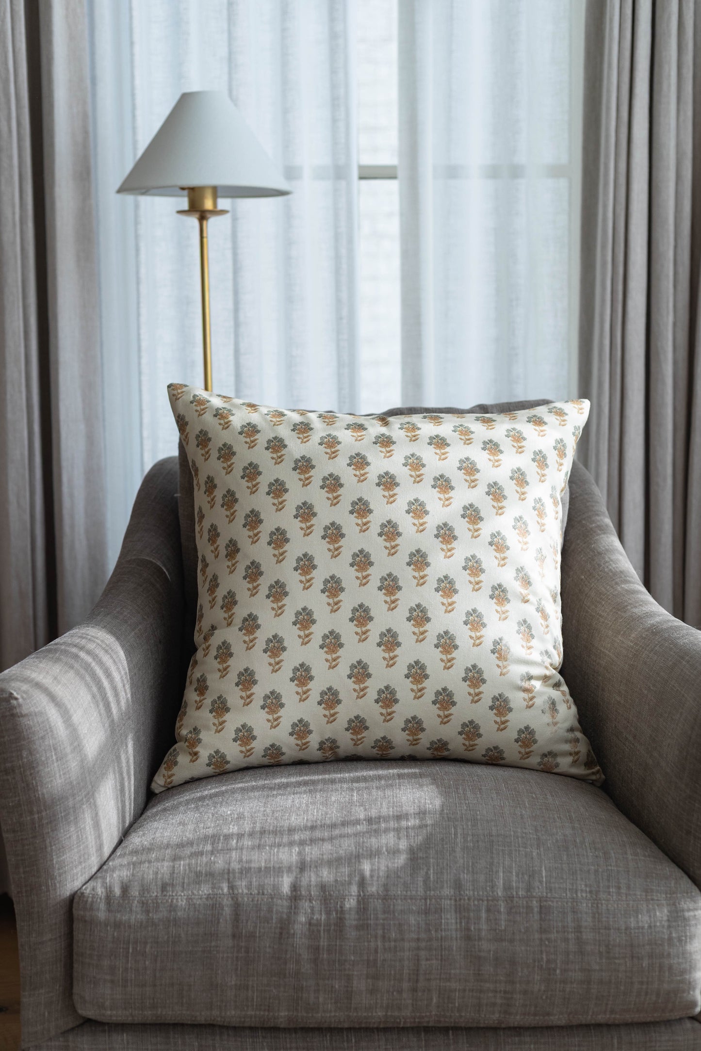 Cream decorative pillow with tan and green floral pattern on gray upholstered chair.