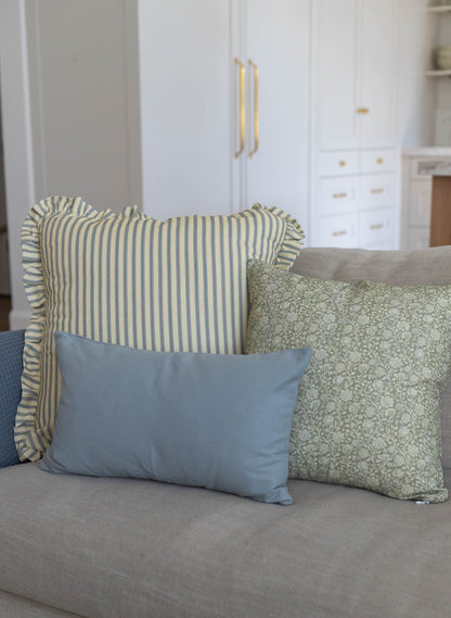 Three decorative pillows on a gray sofa: striped ruffle-edged pillow, solid blue pillow, and green patterned pillow.
