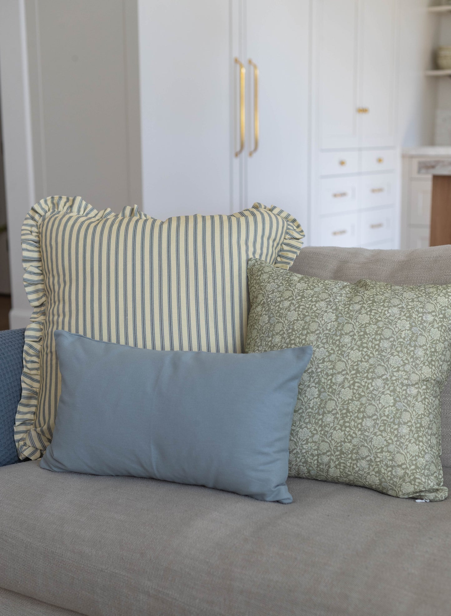 Striped and patterned throw pillows with ruffled edges arranged on a gray upholstered sofa.