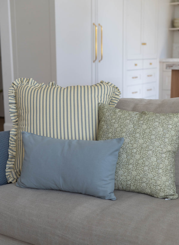 Striped and patterned throw pillows with ruffled edges arranged on a gray upholstered sofa.