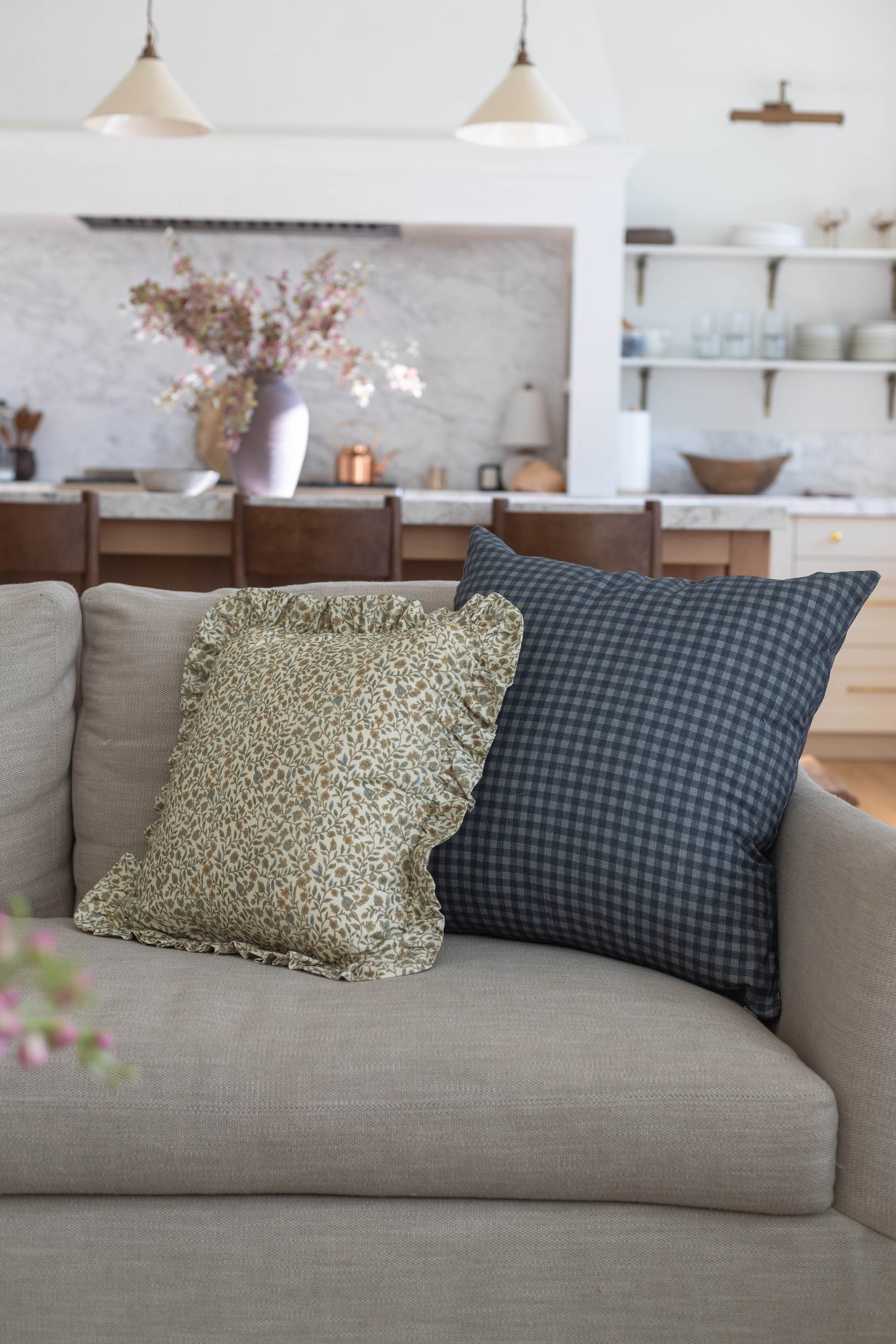 Navy blue gingham checkered pillow with ruffle edge on beige sofa.