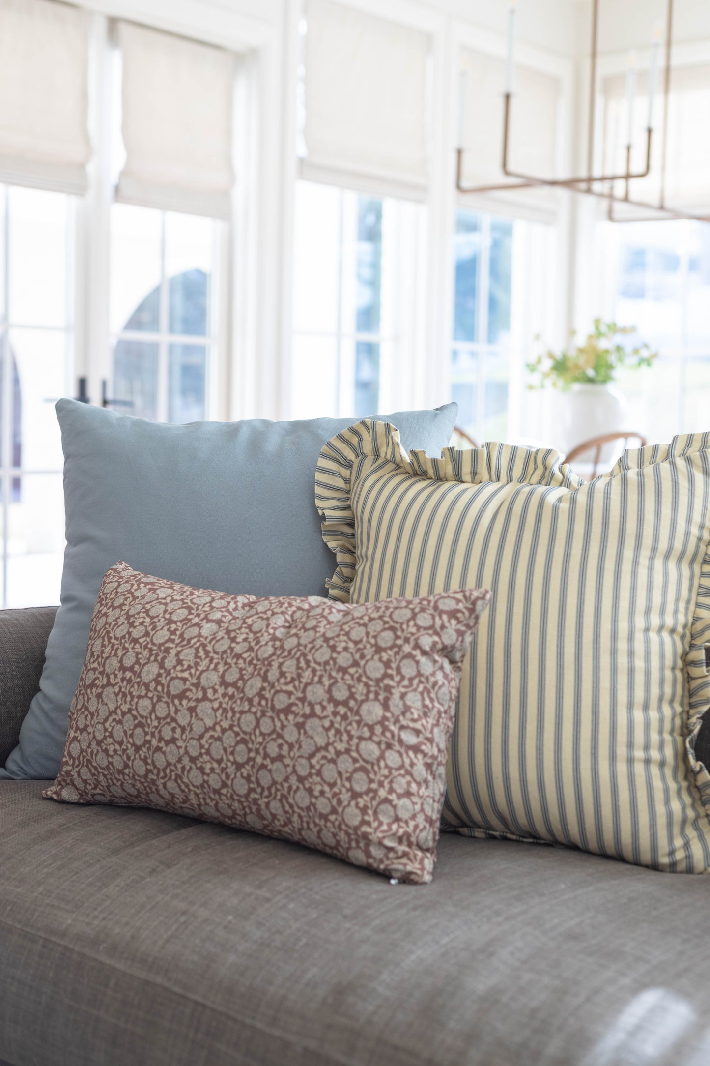 Three decorative pillows on gray sofa: solid blue, yellow striped with ruffle edge, and mauve patterned.