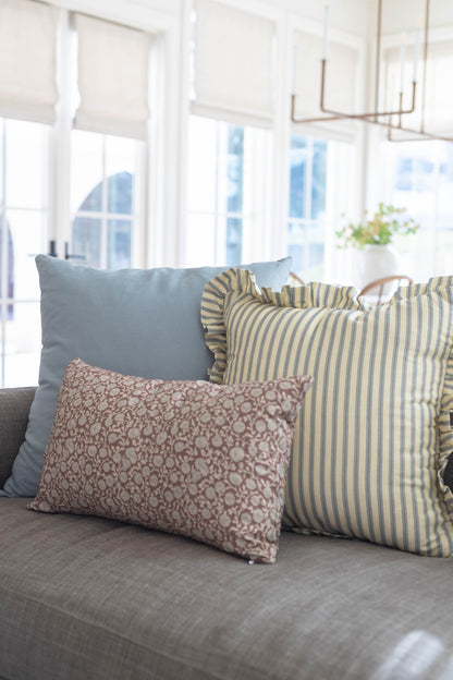 Three decorative pillows on gray sofa: solid blue, yellow striped with ruffle edge, and mauve patterned.