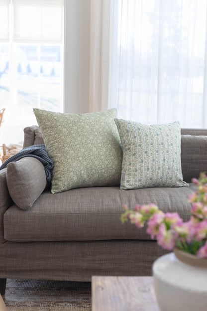 Gray upholstered sofa with green and blue patterned throw pillows near a window.