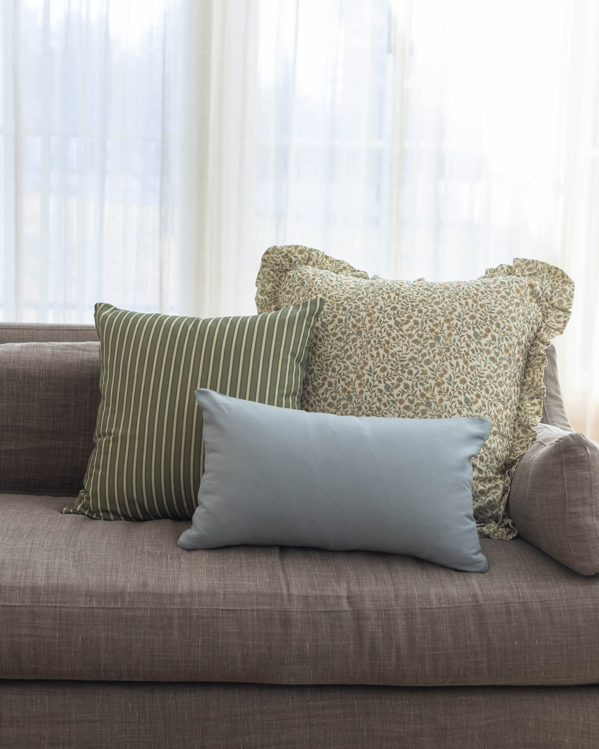 Light blue rectangular pillow displayed on gray sofa with striped and patterned pillows.