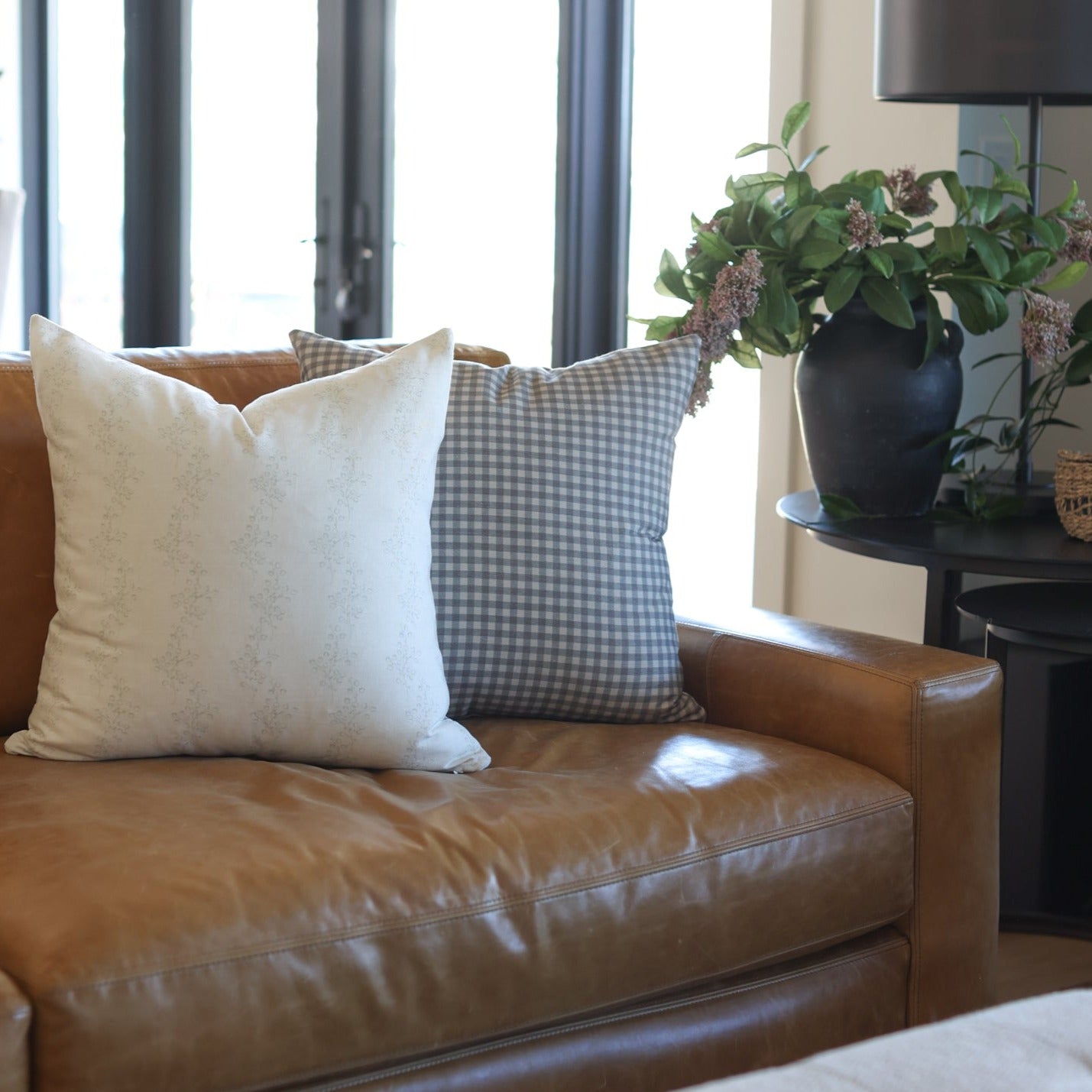 Gray and white gingham check decorative pillow displayed on a brown leather chair.