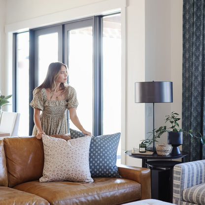 Gray textured curtain panel hanging beside large windows in a living room with furniture.