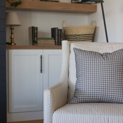 Gray and white gingham check pillow on a striped cream upholstered chair.